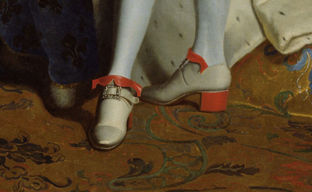 Close-up detail of the footwear in Hyacinthe Rigaud's portrait of Louis XIV, showing white silk shoes with red heels, diamond buckles, and red ribbons on an ornate carpet.